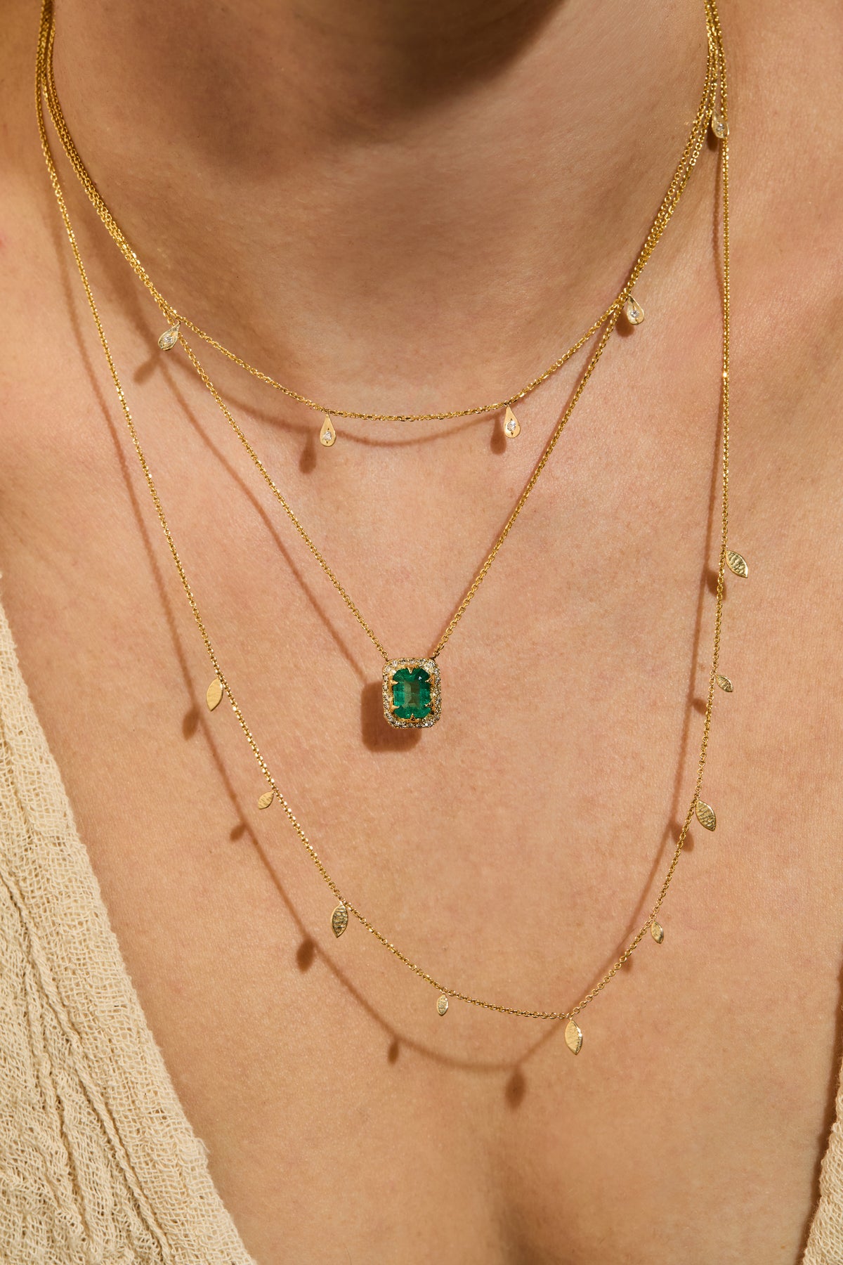 Diamond drop necklace in 14k gold worn over the collarbone with emerald pendant necklace