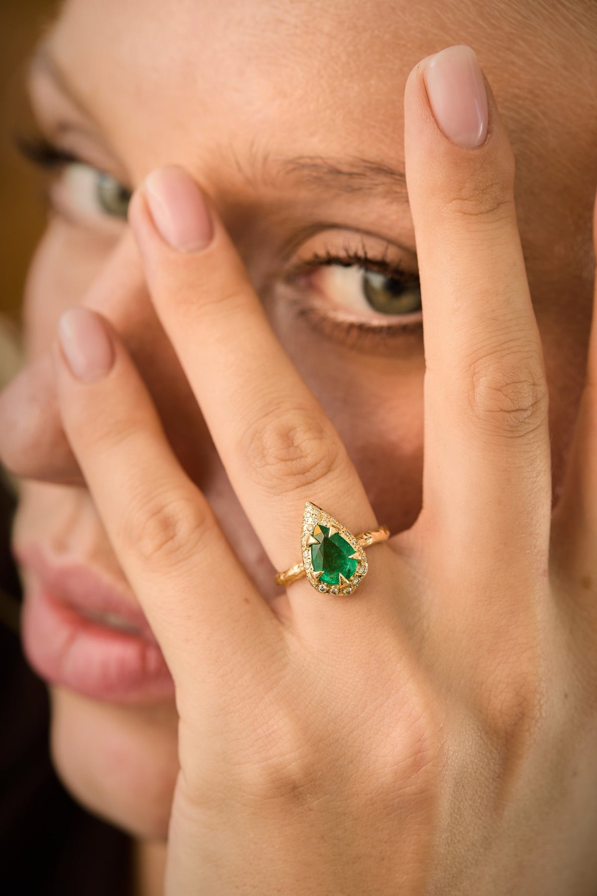 mystic ring with pear-shaped natural emerald, natural diamond detailing and hand-carved textured 14K yellow gold band on hand of model
