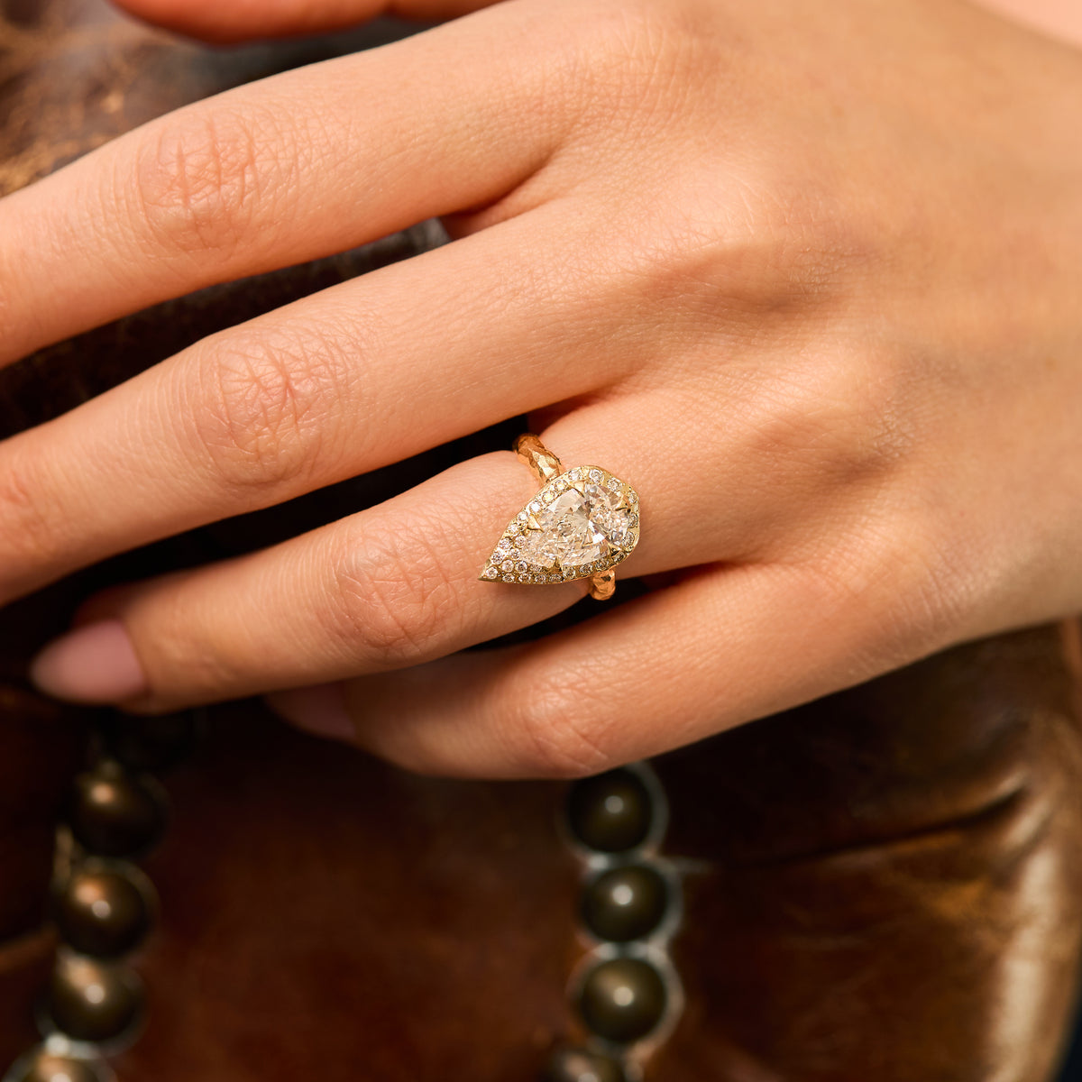 ring with 2 CT pear-shaped natural diamond engagement with diamond halo and hand-carved organic gold band on finger.