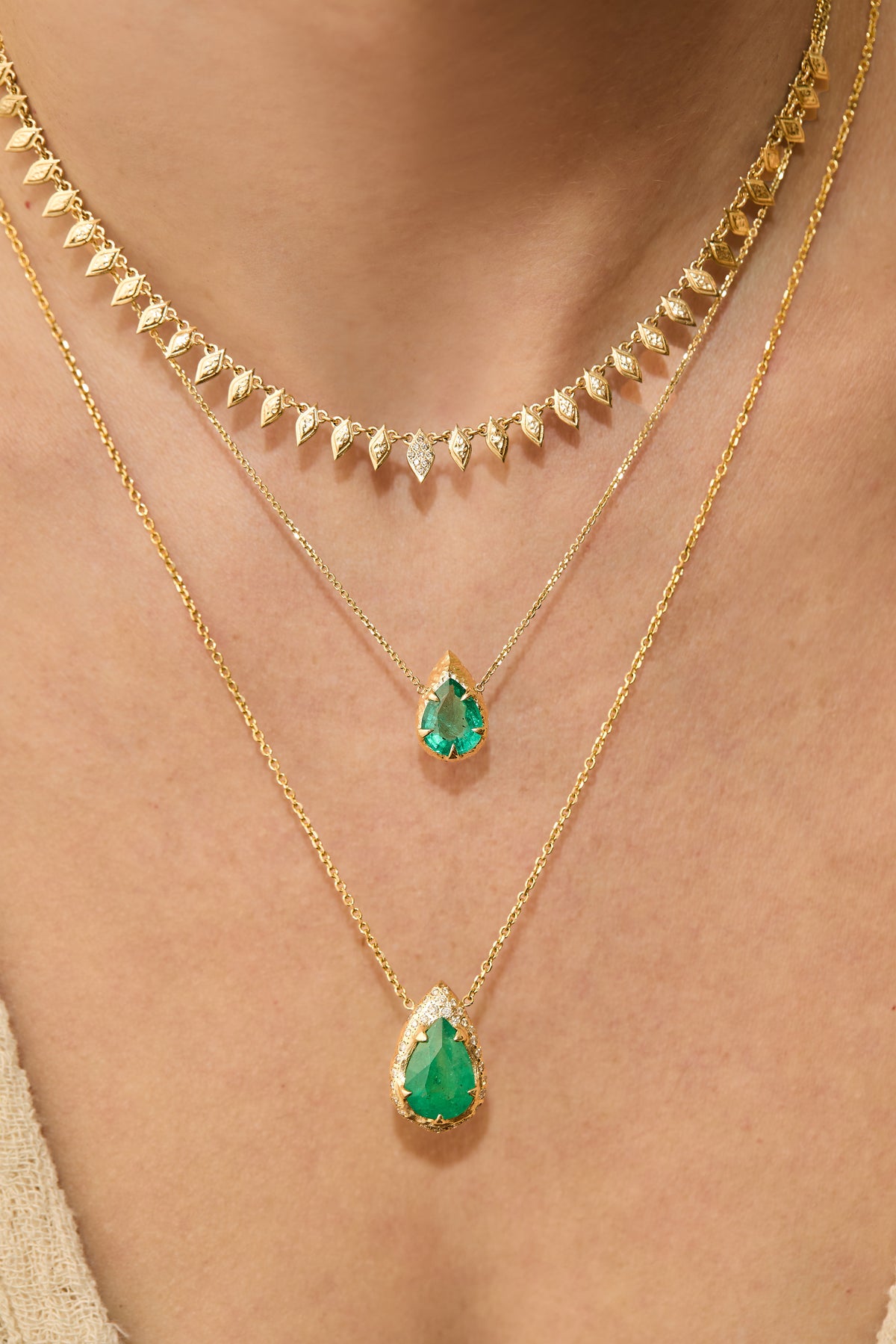 Pear-cut natural emerald drop necklace with hand-carved textured 14K yellow gold setting and delicate gold chain worn on neck with summer necklace and mystic emerald necklace