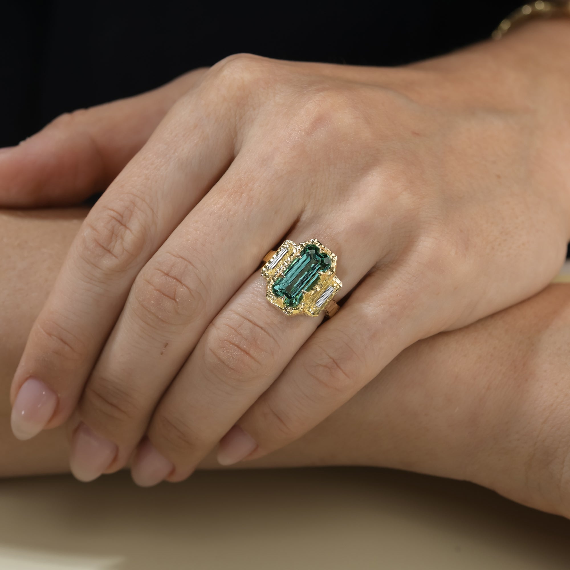 One-of-a-kind lagoon tourmaline ring with baguette side diamonds and textured 14K yellow gold worn on hand.
