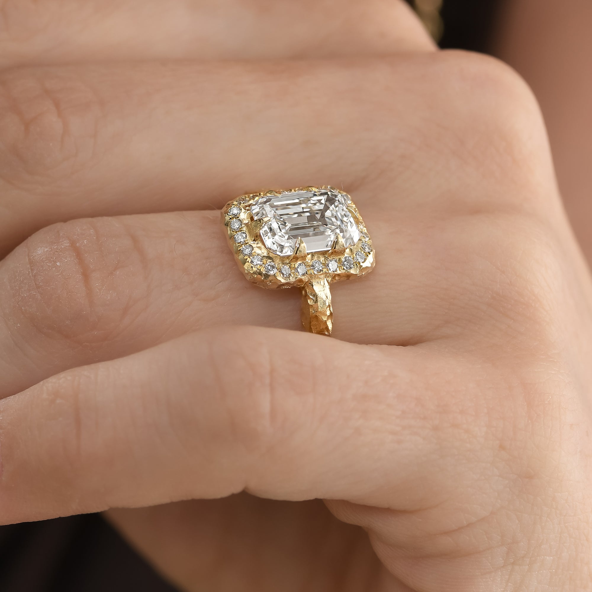 side view of emerald-cut center diamond surrounded by a delicate natural diamond halo in hand-carved 14K yellow gold.