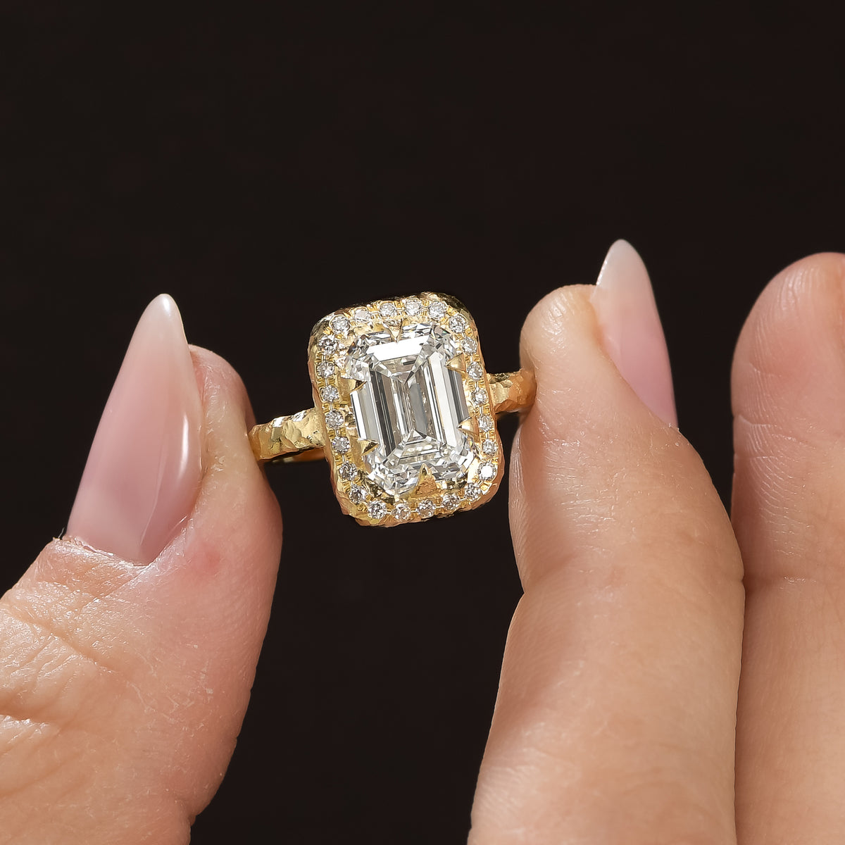 4 ct emerald-cut diamond engagement ring with brilliant-cut diamond halo and sculptural 14K yellow gold setting in between fingers