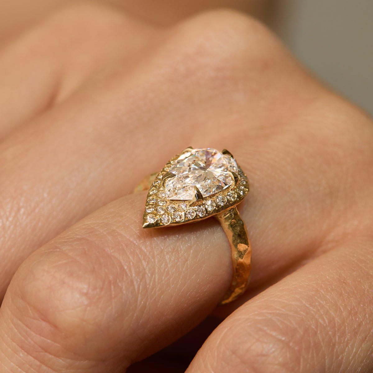 ring with 2 CT pear-shaped natural diamond engagement with diamond halo and hand-carved organic gold band on hand.