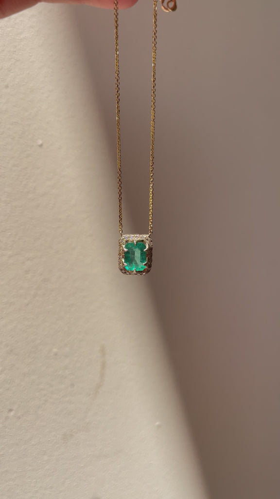North-South emerald-cut emerald necklace featuring a vibrant green emerald, diamond halo and delicate 14K yellow gold chain, shown on the neckline.